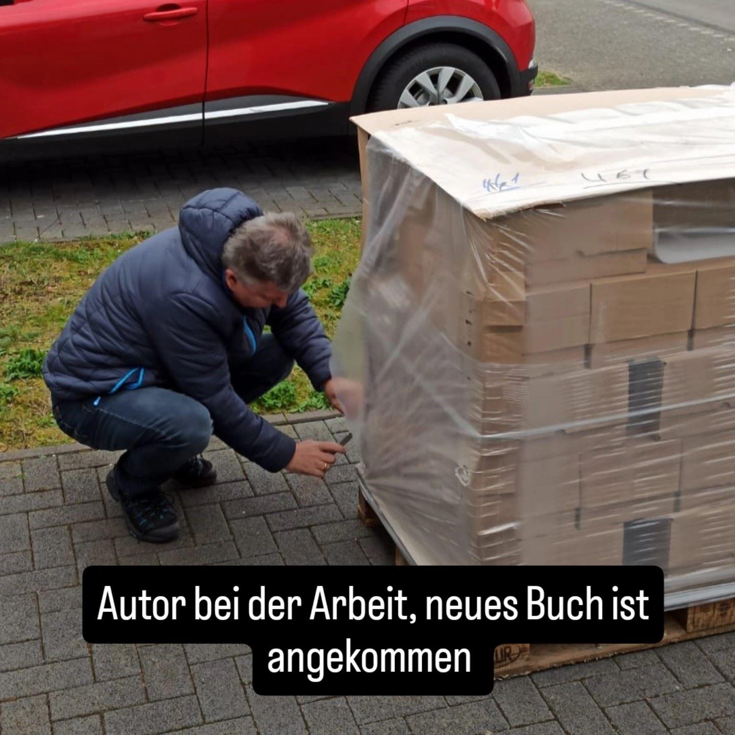 Der Autor in einer blauen Jacke hockend vor einer Palette mit Büchern, von der er die Transportfolie entfernt.