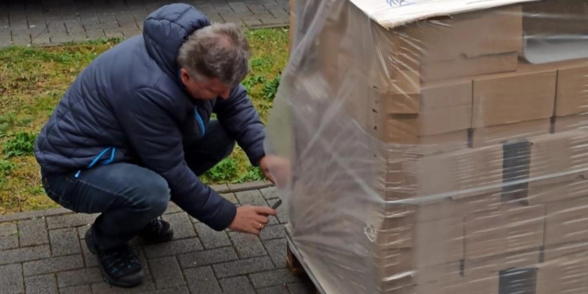 Der Autor in einer blauen Jacke hockend vor einer Palette mit Büchern, von der er die Transportfolie entfernt.